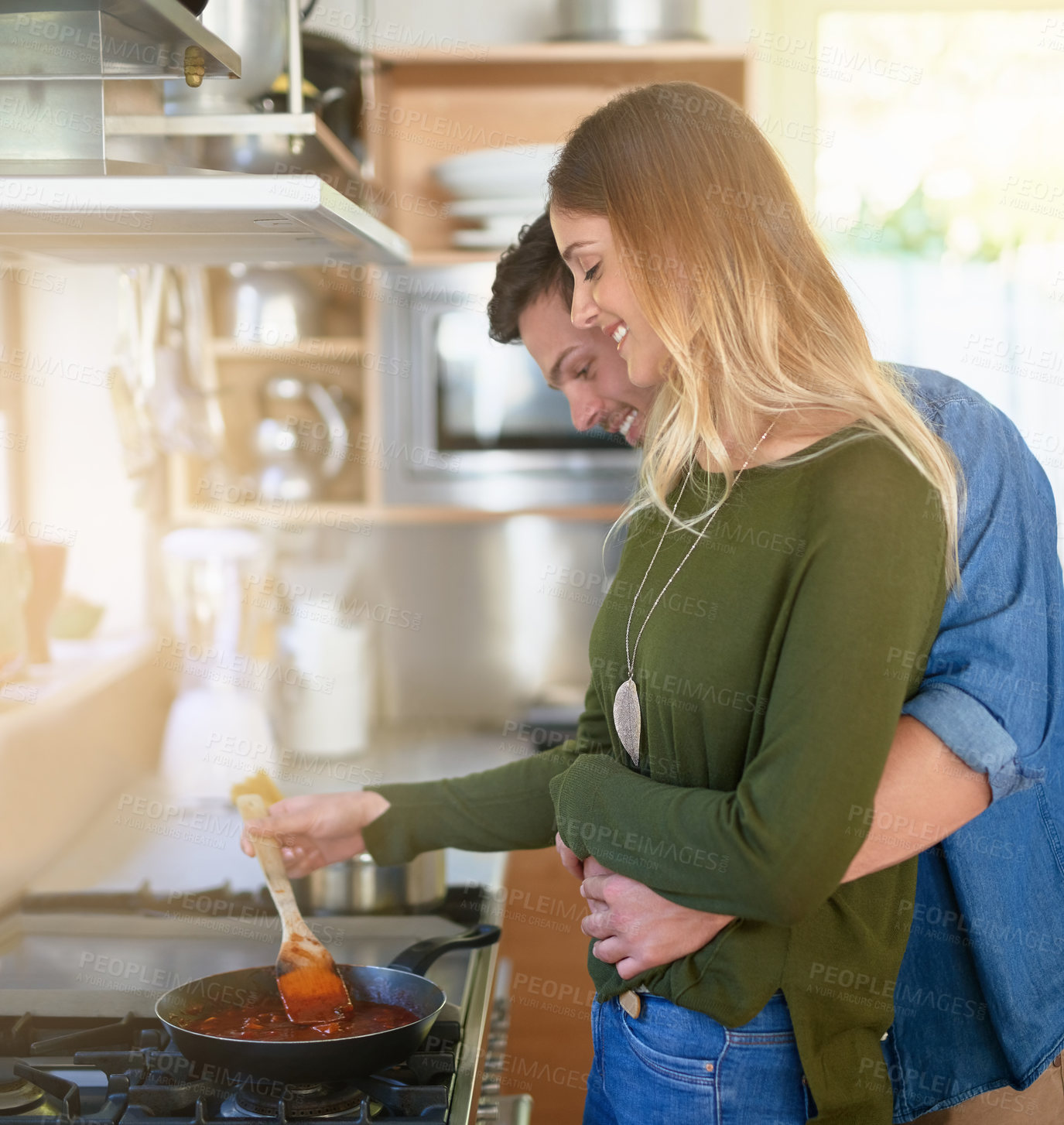 Buy stock photo Shot of an affectionate young couple preparing dinner together at the stove in their kitchen