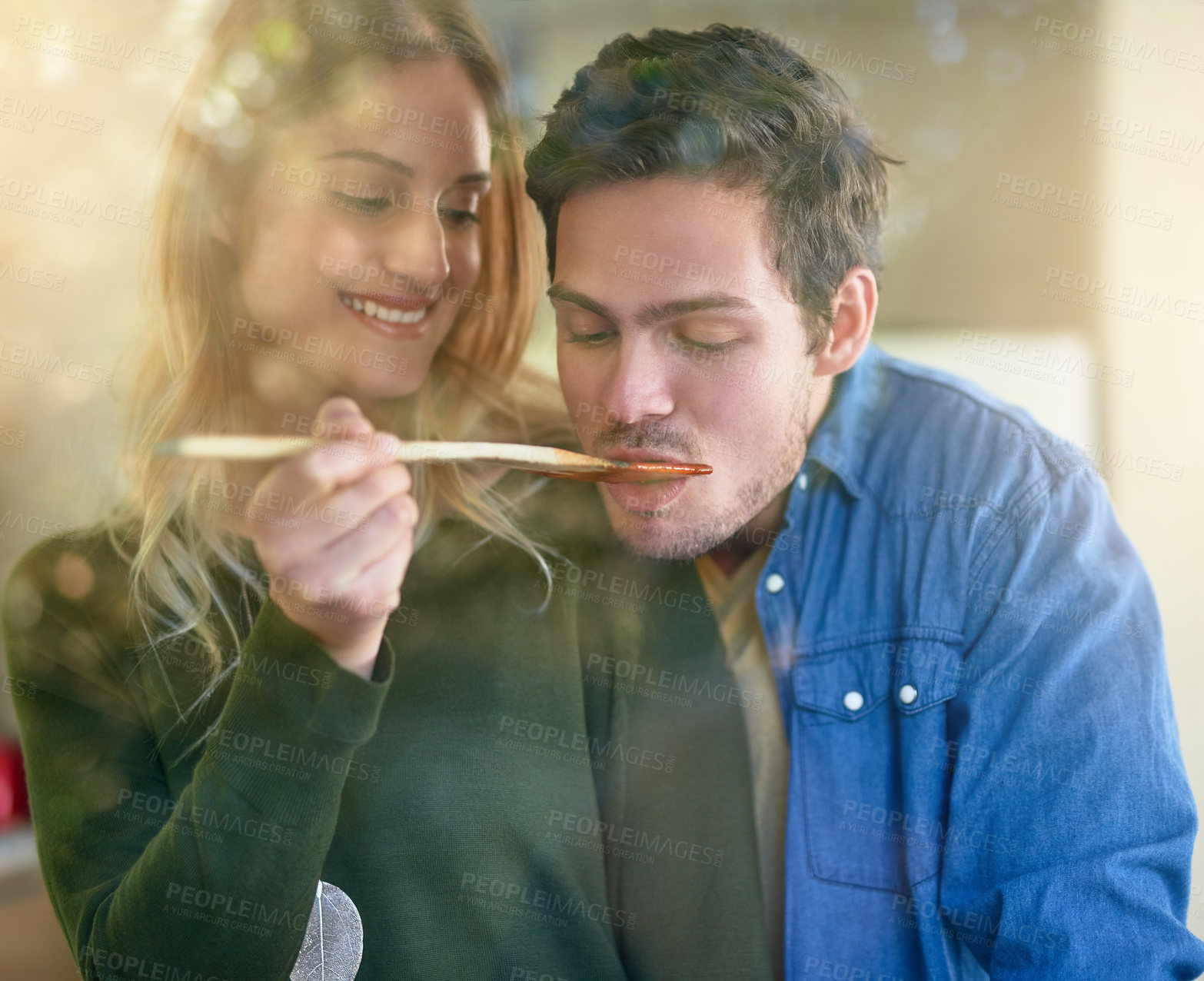 Buy stock photo Shot of an affectionate young couple tasting a sauce they are preparing together in their kitchen