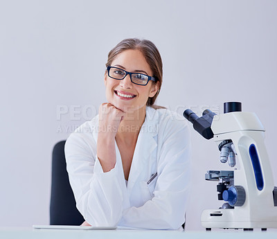Buy stock photo Portrait of a smiling scientist sitting next to a microscope at a desk in a laboratory