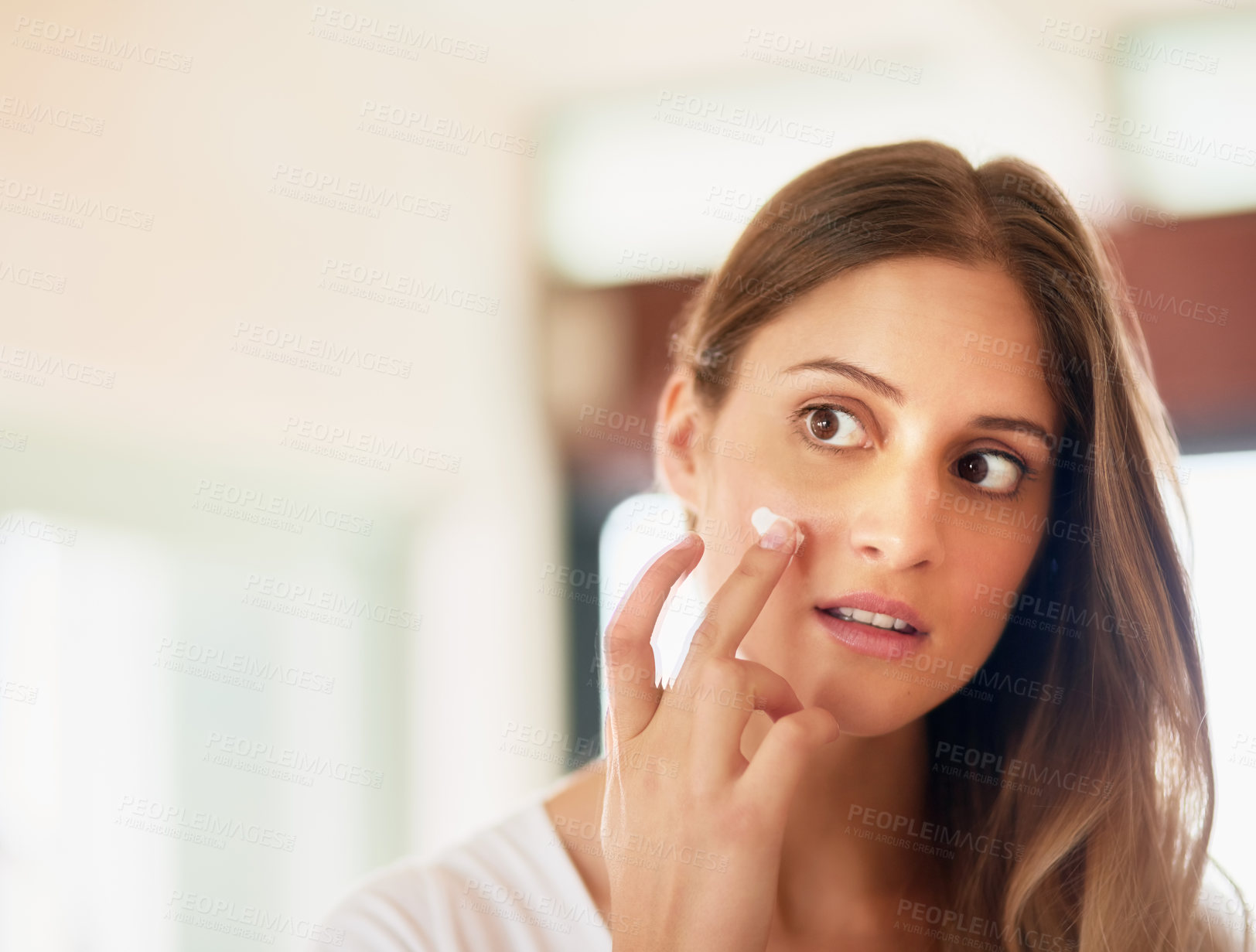 Buy stock photo Cropped shot of a young woman applying moisturiser to her face