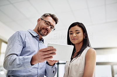 Buy stock photo Cropped shot of a businessman showing something to his colleague on his tablet in the office