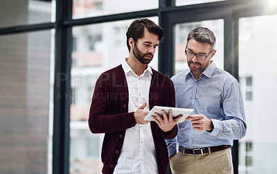 Buy stock photo Cropped shot of a businessman showing something to his colleague on his tablet in the office