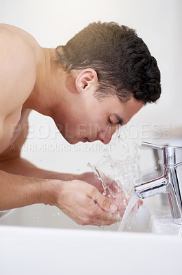 Buy stock photo Shot of a handsome young man washing his face at the bathroom sink
