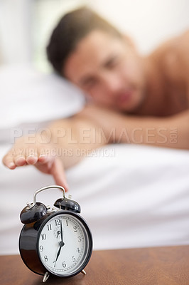Buy stock photo Shot of a young man reaching for his alarm clock in the morning