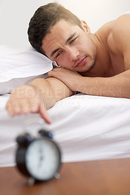 Buy stock photo Shot of a young man reaching for his alarm clock in the morning