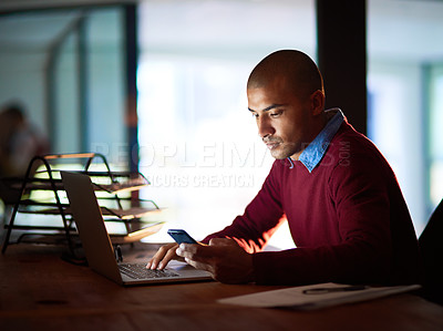 Buy stock photo Shot of a handsome young man sending a text while working late in his office
