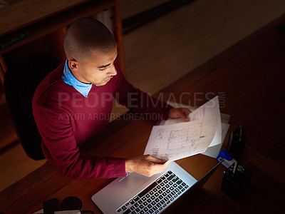 Buy stock photo High angle shot of a young man reading paperwork while working late in the office