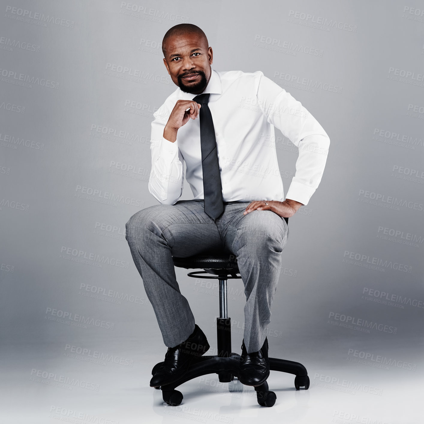 Buy stock photo Studio portrait of a corporate businessman sitting on a chair against a grey background