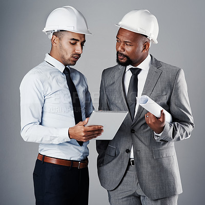 Buy stock photo Shot of two civil engineers discussing building plans while standing in the studio