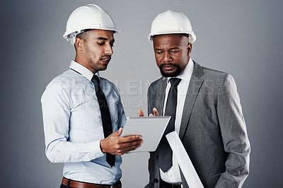 Buy stock photo Shot of two civil engineers discussing building plans while standing in the studio