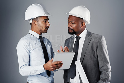 Buy stock photo Shot of two civil engineers discussing building plans while standing in the studio