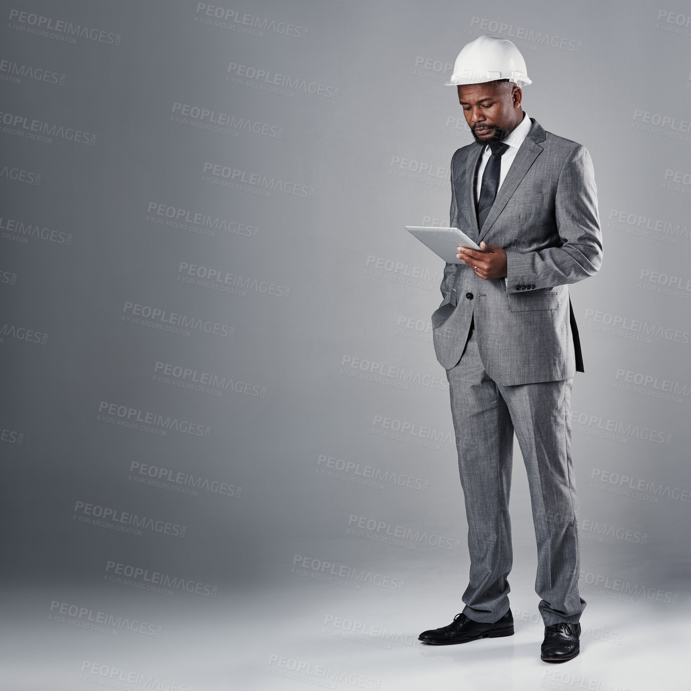 Buy stock photo Shot of a well-dressed civil engineer using his tablet while standing in the studio