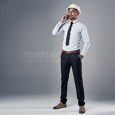 Buy stock photo Shot of a well-dressed civil engineer using his cellphone while standing in the studio