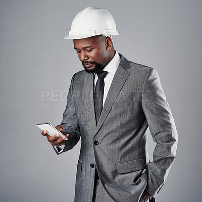 Buy stock photo Shot of a well-dressed civil engineer using his cellphone while standing in the studio