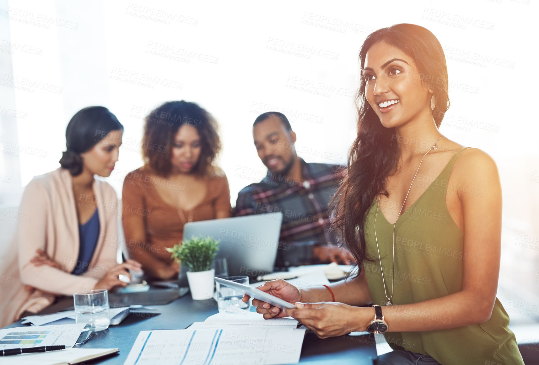 Buy stock photo Shot of a young woman using a digital tablet during a meeting with her colleagues in the background