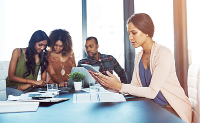 Buy stock photo Shot of a young woman using a digital tablet during a meeting with her colleagues in the background