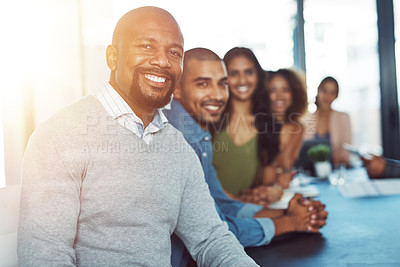Buy stock photo Portrait of a businessman sitting in a boardroom with his colleagues blurred out in the background