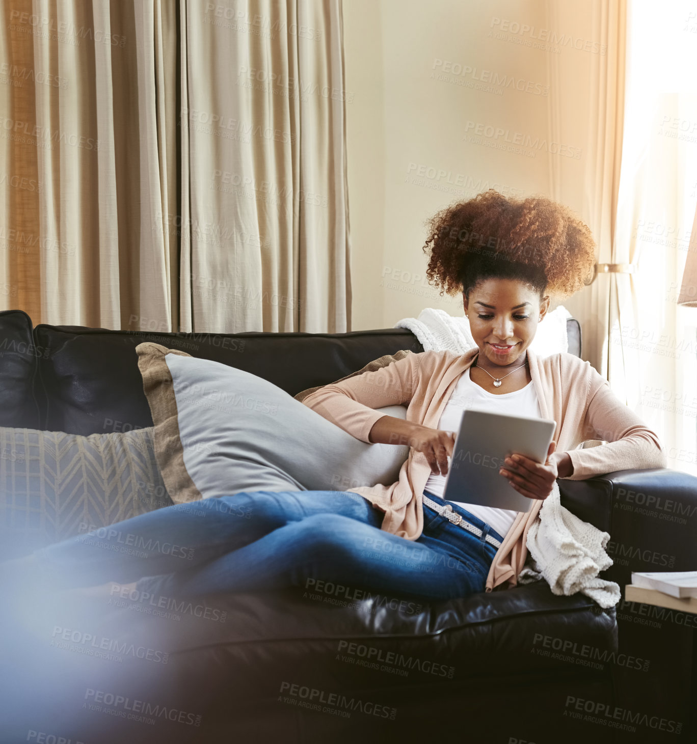 Buy stock photo Shot of an attractive young woman using her tablet while chilling at home on the sofa