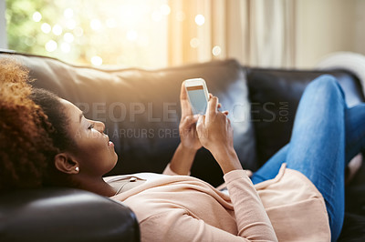 Buy stock photo Shot of an attractive young woman using her cellphpone while chilling at home on the sofa