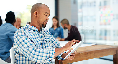 Buy stock photo Shot of a handsome young man using his tablet while sitting in the boardroom during a meeting