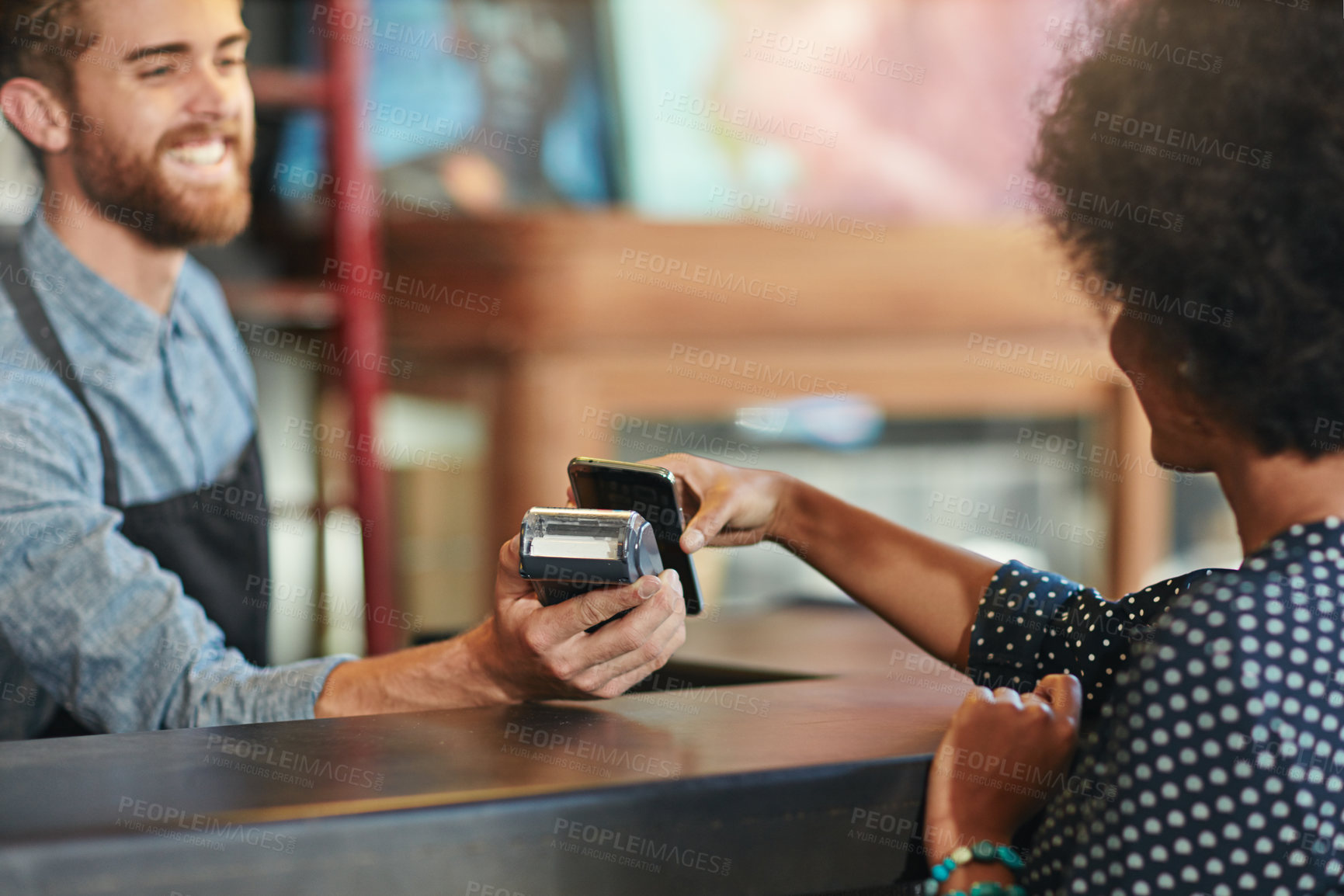 Buy stock photo Shot of a barista taking a smartphone payment from a customer at a cafe