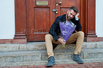 Buy stock photo Shot of a handsome young man looking depressed while waiting with a bunch of flowers on a step