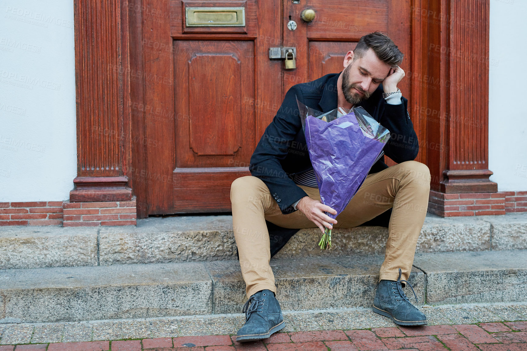 Buy stock photo Shot of a handsome young man looking depressed while waiting with a bunch of flowers on a step