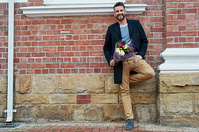 Buy stock photo Portrait of a handsome young man standing against a brick wall with a bunch of flowers in hand