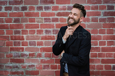 Buy stock photo Cropped shot of a handsome young man looking thoughtful while standing against a brick wall outside