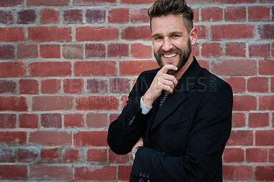 Buy stock photo Portrait of a handsome young man standing against a brick wall outside