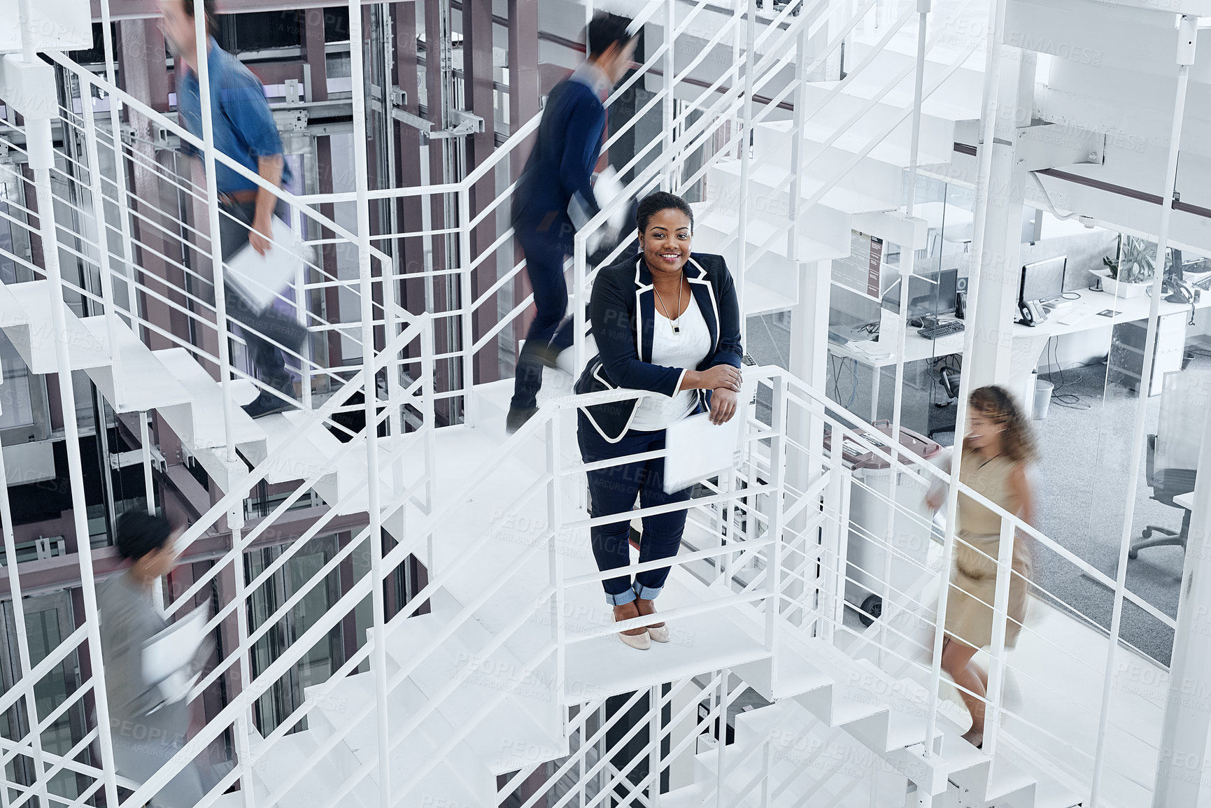 Buy stock photo Portrait of a young professional standing on a stairs with colleagues rushing around her