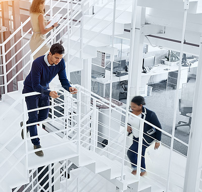 Buy stock photo Shot of a young professional standing on a stairs with colleagues rushing around him