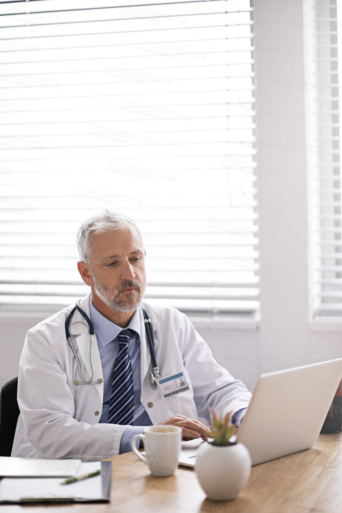 Buy stock photo Cropped shot of a mature male doctor working at his desk