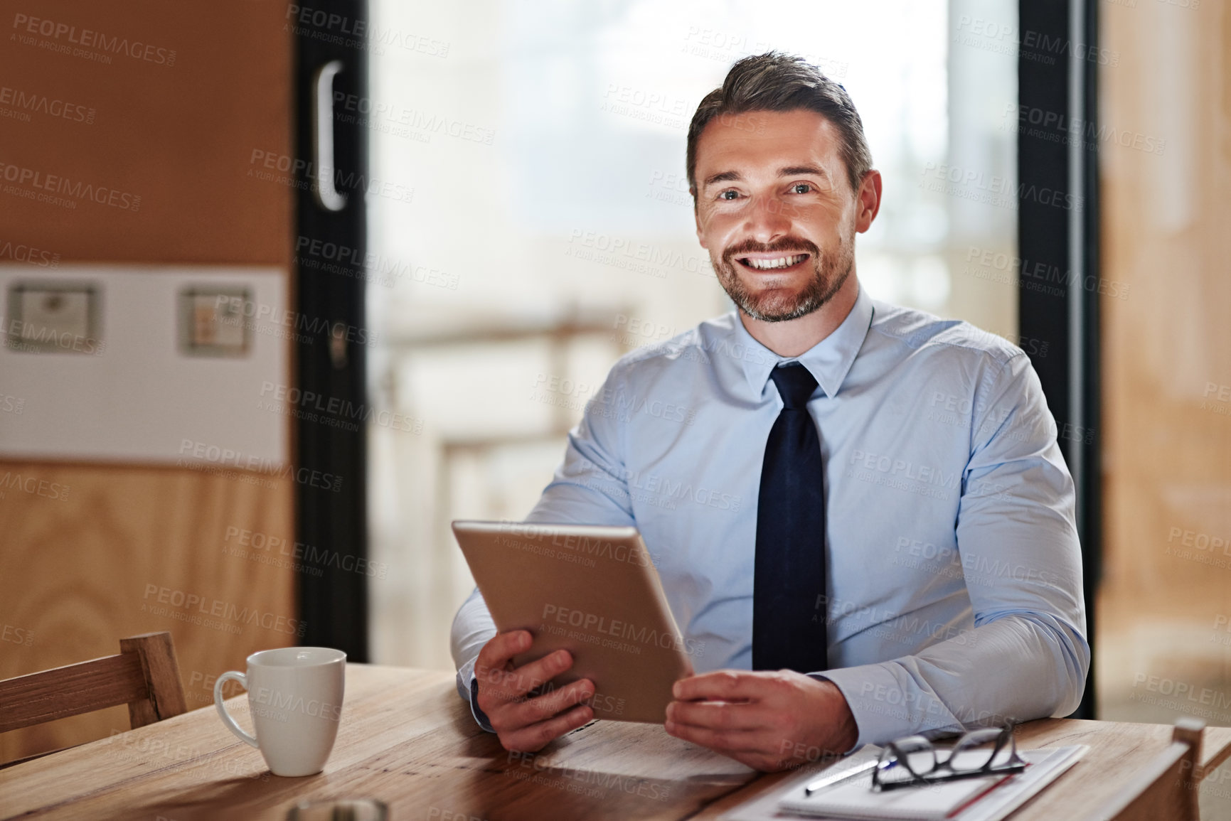 Buy stock photo Shot of a smiling businessman using a digital tablet in an office