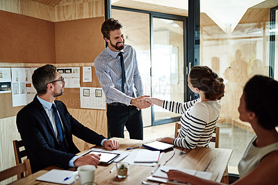Buy stock photo Shot of two colleagues shaking hands together in an office while colleagues look on