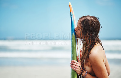 Buy stock photo Shot of an attractive young woman standing on a beach kissing her surfboard