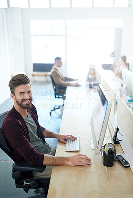 Buy stock photo Portrait of a young designer sitting at his workstation with a colleague in the background