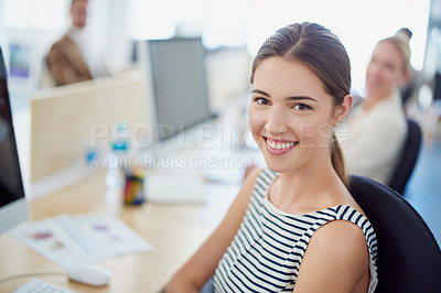 Buy stock photo Portrait of a young designer sitting at her workstation with colleagues in the background