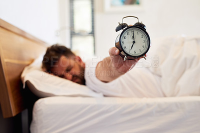 Buy stock photo Cropped shot of a young man holding up an alarm clock while waking up from bed at home