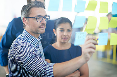 Buy stock photo Cropped shot of a handsome businessman making notes on a glass wall while his colleagues look on