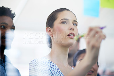 Buy stock photo Cropped shot of an attractive young businesswoman making notes on a glass wall while her colleagues look on