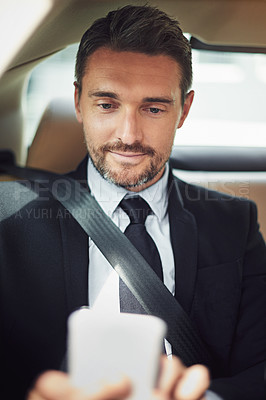 Buy stock photo Shot of a businessman using his phone while traveling in a car