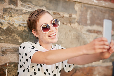 Buy stock photo Shot of a trendy young woman using her phone while leaning against a wall outside