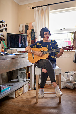 Buy stock photo Shot of a stylish young woman sitting in her eclectic toom playing a guitar