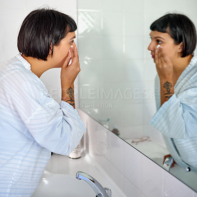 Buy stock photo Shot of a young woman in a bathrobe cleaning her face in her bathroom mirror in the morning