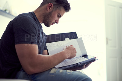 Buy stock photo Shot of a confident young man studying some paperwork while sitting on his bed at home