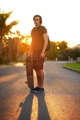 Buy stock photo Portrait, man and skateboard in outdoor, street and backpack on headphones, summer and sunset. University student, physical activity and sports in urban, skater and athletic in edgy, exercise and fun