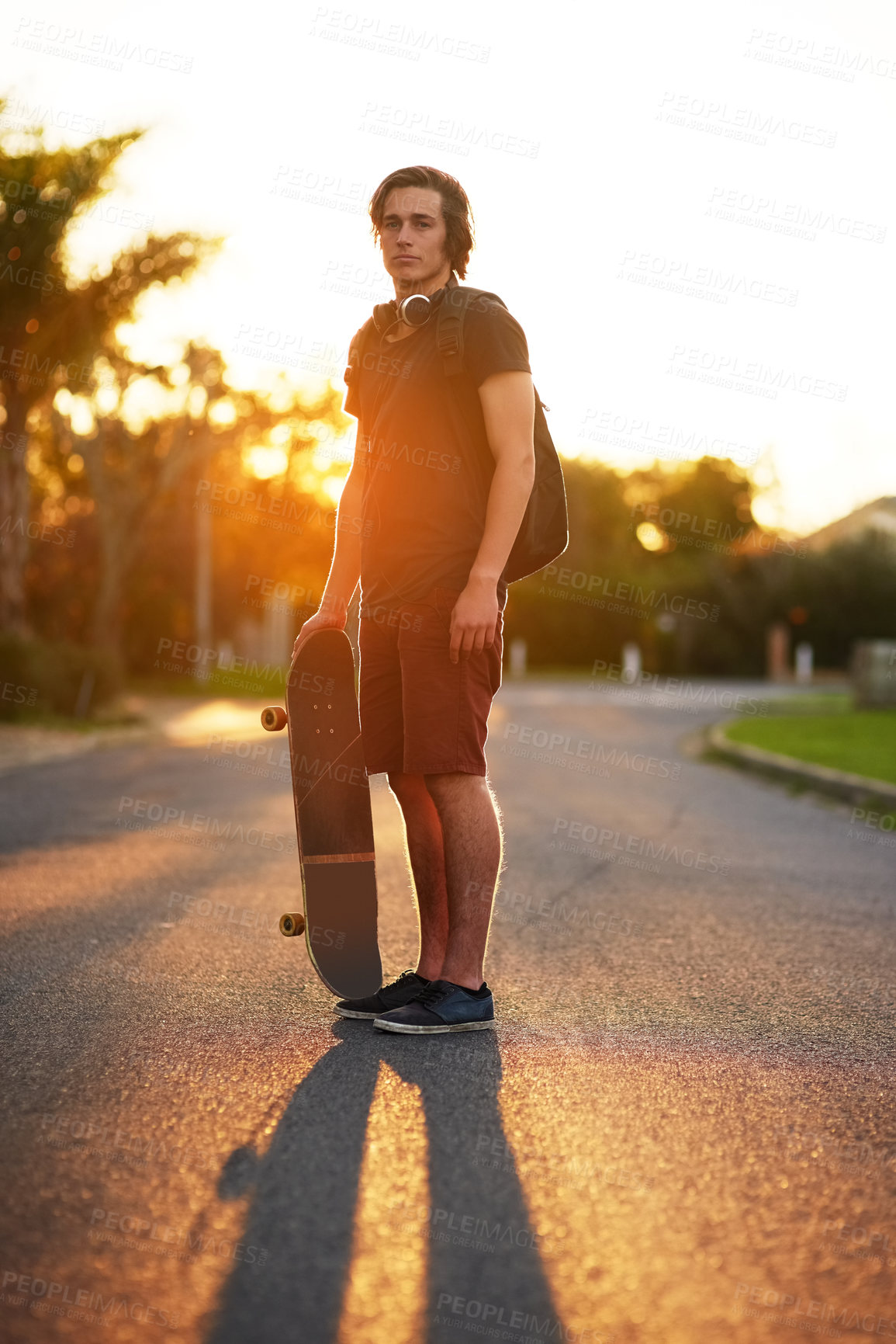 Buy stock photo Portrait, man and skateboard in outdoor, street and backpack on headphones, summer and sunset. University student, physical activity and sports in urban, skater and athletic in edgy, exercise and fun