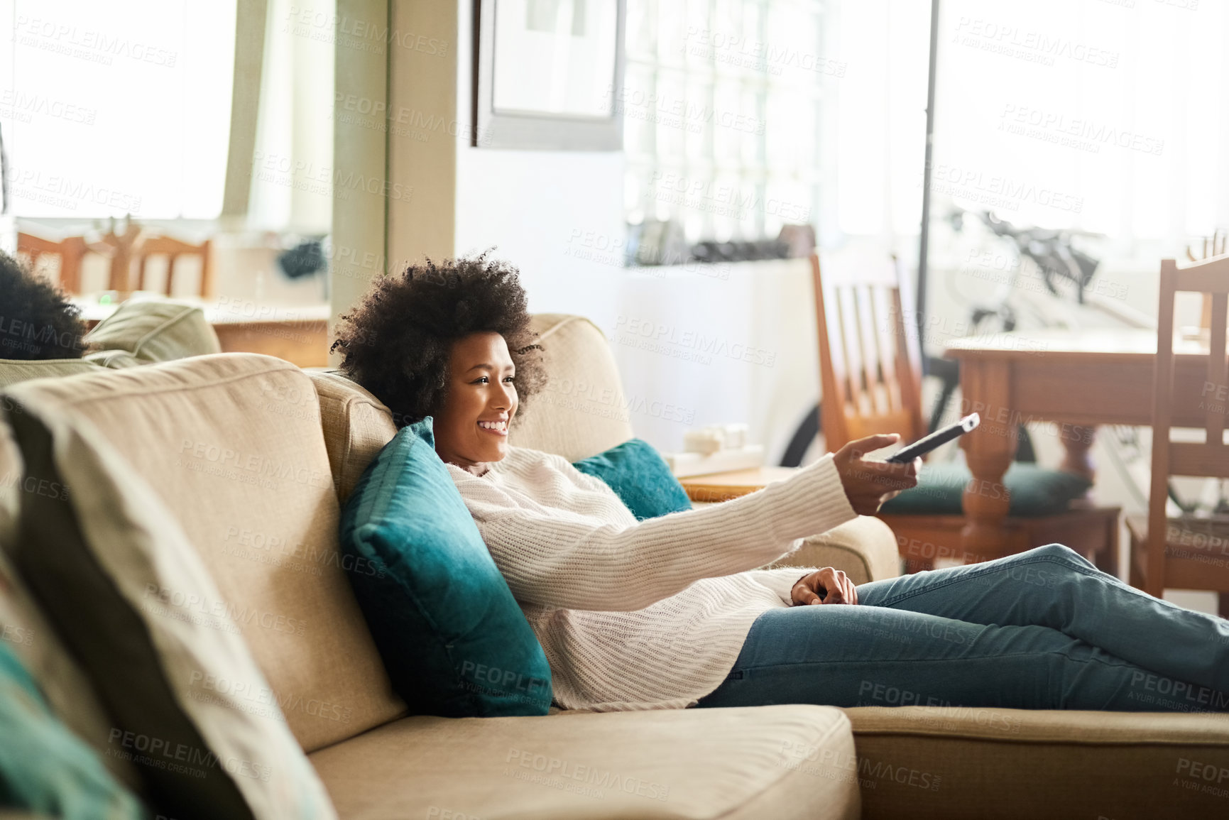 Buy stock photo Shot of a young woman relaxing on the sofa at home and watching tv