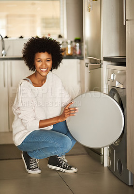 Buy stock photo Shot of a young woman doing laundry with a washing machine at home